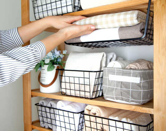 Bed sheets, duvet covers and towels are folded vertically. Metal and fabric black baskets. The concept of housework and storage.